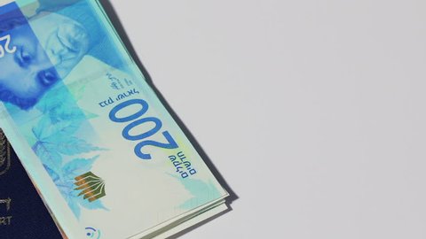 Stack of israeli money bills of 200 shekel and israeli passport - Pan left