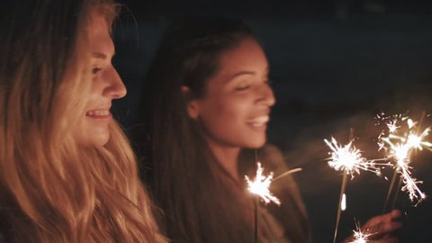 Friends light sparklers on beach party for new years fun vacation summer holiday celebration laughing and smiling together for carefree lifestyle.