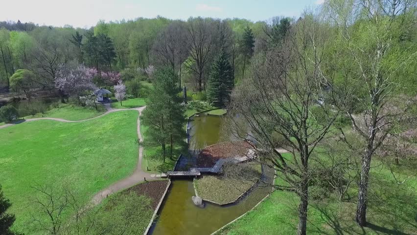 Path with wooden plates over pond and small island in japan garden at sunny spring day. Aerial view