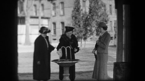 SARATOGA SPRINGS, NY 1938: Women filling water bottles from public fountain in formal period dress.
