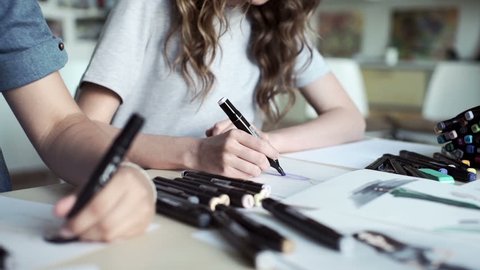 Designers draw sketches in the Studio. two attractive women working and smiling. Workspace designer. White sheet of paper, pencils, markers, felt-tip pens.