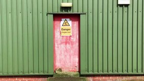 Establishing clip of a red door in a green metal wall with a fragile roof warning sign 