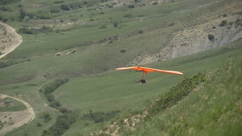 Red hang glider flying close to the camera in the background of grape fields