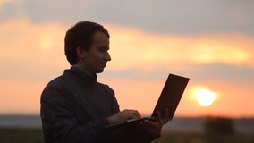 A man makes a video call on a laptop. Beautiful sunset on the background