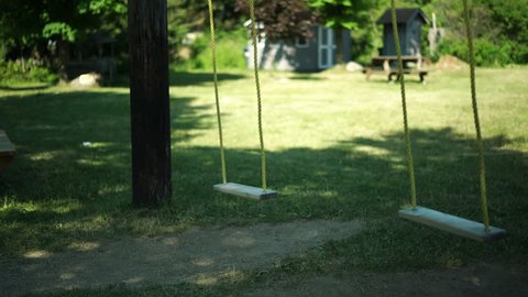 Two wooden swing seats swaying gently back and forth in the before noon breeze. Shallow depth of field.
