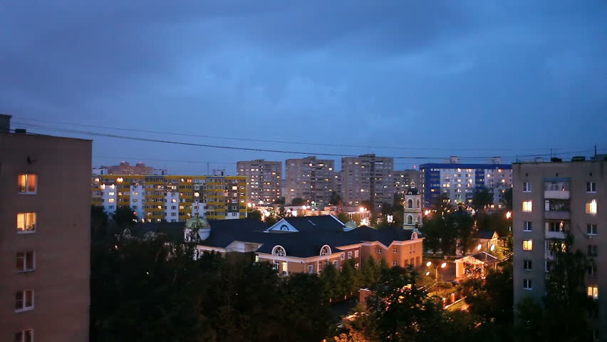 Heavy rain with thunderstorm in the city. Sometimes a flash of lightning. Night cityscape.