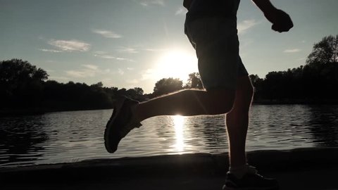 Super slow motion steadicam clip of sunset park runner on pond bank. Bleached