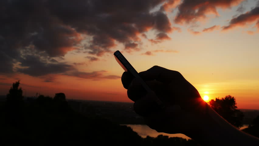 Man talking by mobile phone on sunset sky background