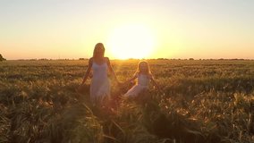 The young woman with the girl go to the field of wheat at sunset

