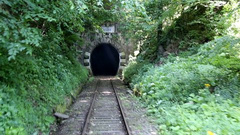 Back view of railroad train that entering a dark and old mountain tunnel. Inaugurated in 1863, it is the oldest mountain railway in Romania. Route between Oravita and Anina. Banat region.
