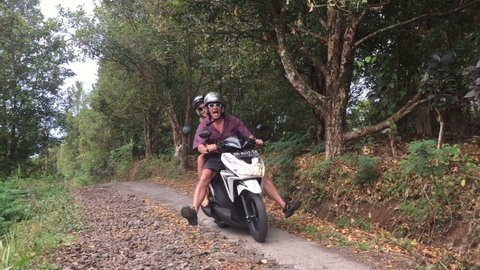 Two people riding a scooter appear to be out of control in the jungle on a very narrow road.