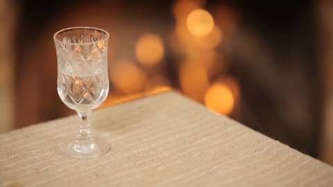 Glass with vodka on a background of a burning fireplace
