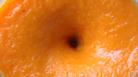 Slow motion close up shot of orange smoothie being made in a blenter. Top view