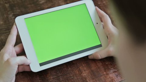 Woman sitting and looking at white digital tablet computer device with blank green display. Mock up, entertainment, copyspace, template, leisure time, chroma key, green screen, technology concept