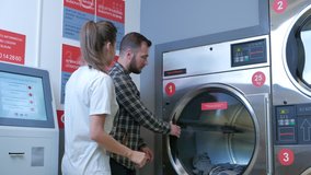Young cheerful couple doing laundry together at laundromat shop in 4k UHD video.