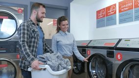 Young cheerful couple doing laundry together at laundromat shop in 4k UHD video.