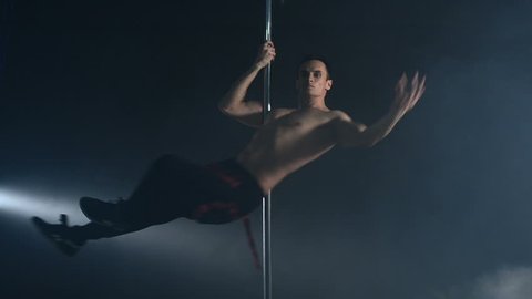 Young strong sexy pole dance man dancing on a black background