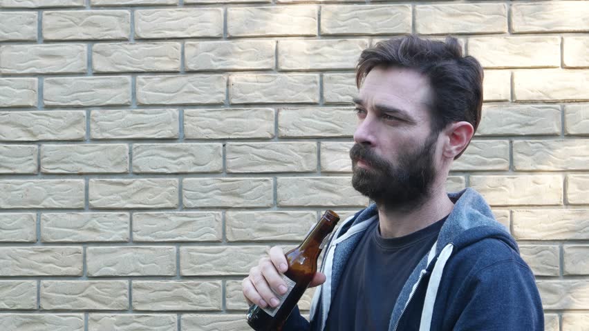 man in front of brick wall drinking on fringes of group