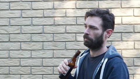 man in front of brick wall drinking on fringes of group