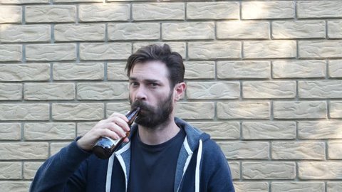 man in front of brick wall drinking with mean look