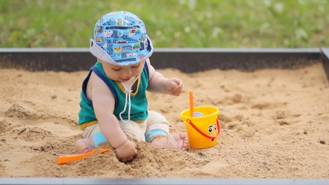 Baby boy digging in the sandbox. Smiles and touches the sand