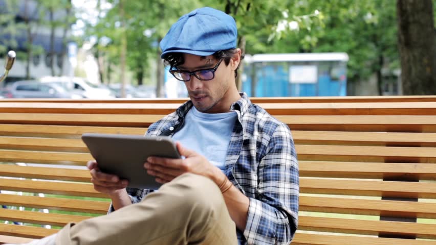 leisure, technology, communication and people concept - creative man with tablet pc computer sitting on city street bench over fixed gear bicycle