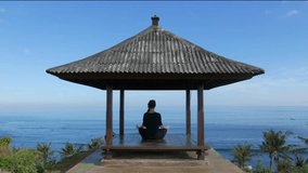 Girl sitting in the lotus position on a sky background. Woman relaxing and doing yoga. Weekend relaxation. Yoga tour. Video output for posters. Woman relaxing with ocean views. Yoga ocean.