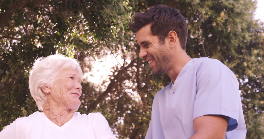 Male nurse assisting a senior woman to walk in the backyard of hospital