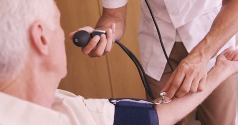 Male doctor checking blood pressure of senior man in hospital