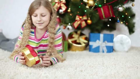 Girl considering a Christmas gift and lying on the floor near Christmas Tree
