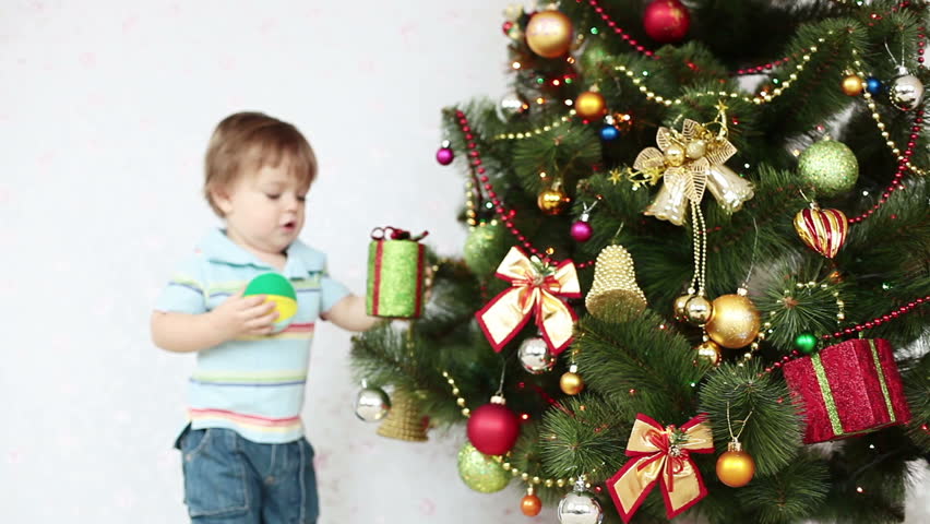 Baby boy holding gifts and standing near a Christmas tree