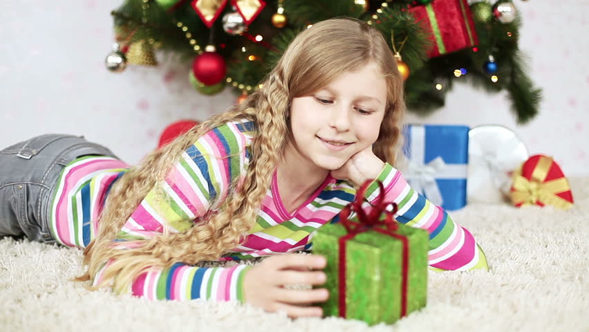 Happy girl with a gift lies near the Christmas Tree
