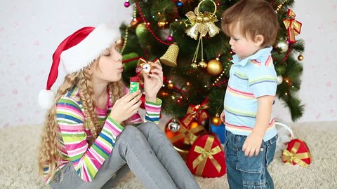 Sister and brother near the Christmas tree. Girl blowing bubbles