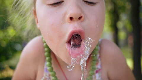 Little child girl funny catch water jet with mouth drink from drinking fountain
