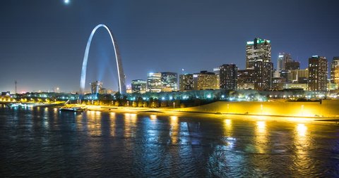 St. Louis, Missouri, USA - view of the illuminated city at night with the Gateway Arch monument and the Mississippi River with passing ship - Timelapse with pan right to left 