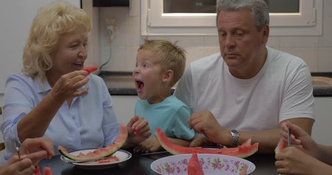Grandmother feeding a little grandchild with watermelon in playful manner