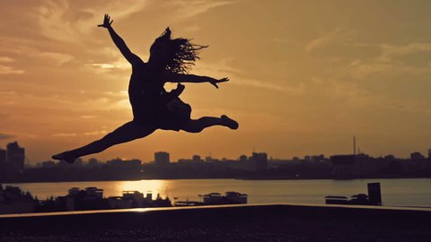 Young attractive girl with flowing hair jumping in dance at sunset silhouette