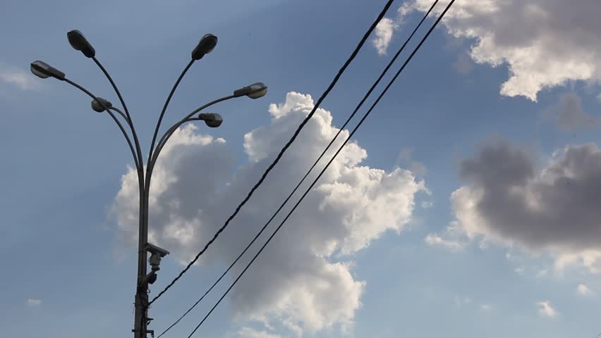 Time lapse clip of white fluffy clouds over blue sky and street lamp with wire