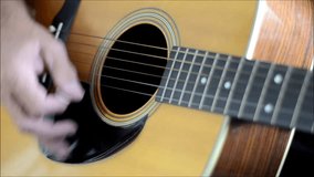 Close up of man playing a wooden acoustic guitar. Lighting from right side of clip