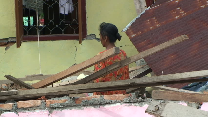 PADANG, INDONESIA - CIRCA OCTOBER 2009: Woman stands outside house damaged by