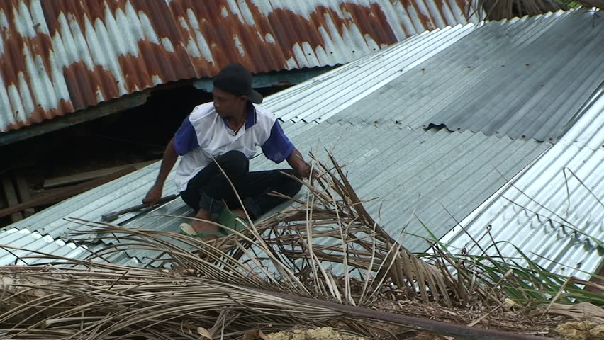 PADANG, INDONESIA - CIRCA OCTOBER 2009: Man attempts to repair house damaged by