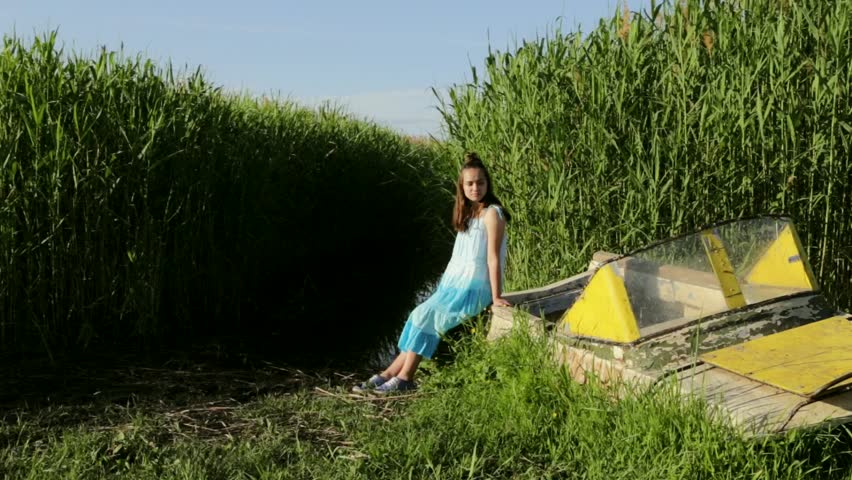 Young teenage girl sitting on old boat near the lake rural green reeds background