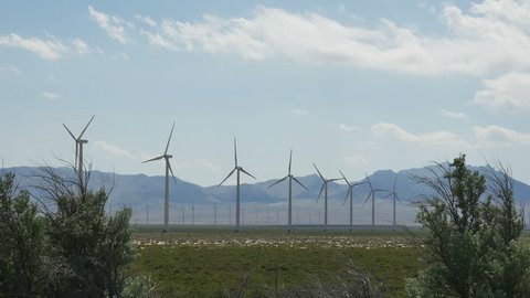GREAT BASIN DESERT, WESTERN UTAH - JUNE 2016: Rows of giant electrical generating wind turbines turn in desert scene framed by tall brush with distant mountains and blue sky with clouds in the desert.