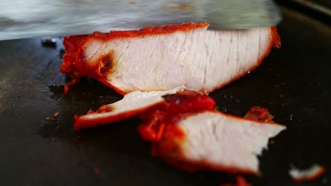 Macro shot in 4K of cutting honey pork with a knife on a wood board. 