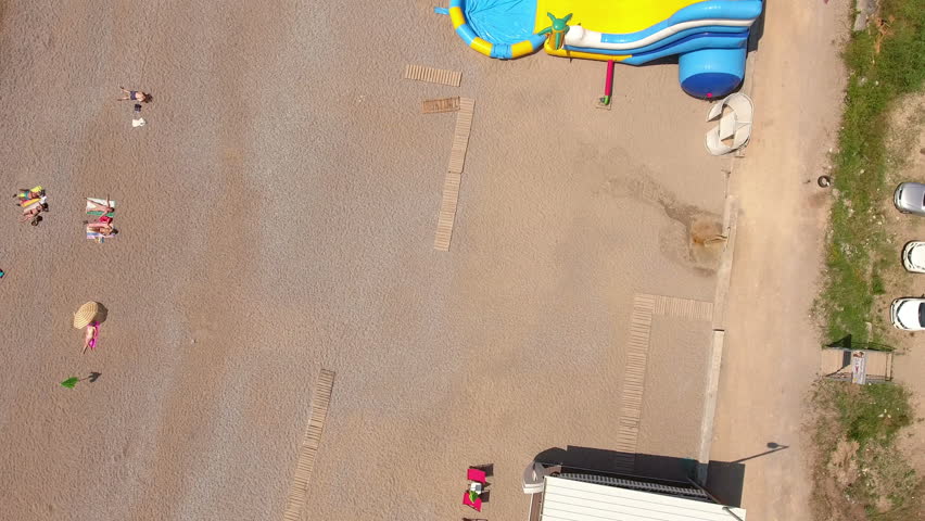 Camera flying up over the Jaz beach with car parking lot and waterfront with sunbeds and parasols. Adriatic sea, Montenegro