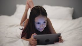 Little girl uses the tablet in bed before going to sleep