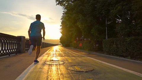Man in blue uniform running on summer sunset embankment along bicycle road, Moscow. Super slow motion steadicam shot at 240 fps