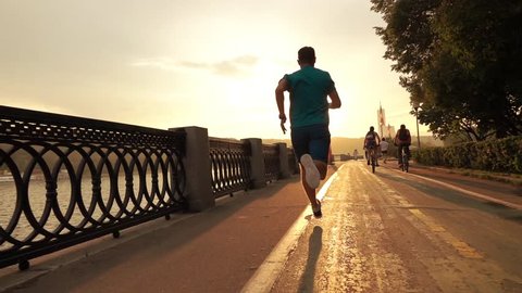 Man in blue running on summer sunset embankment at the camera, Moscow. Super slow motion steadicam shot at 240 fps