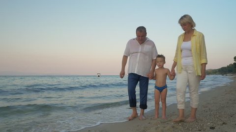 Steadicam shot of grandparents and grandson holding hands and walking barefoot along the shore