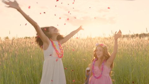 Young girls exploding party cracker in the wheat field and merrily catching the falling confetti during sunset
